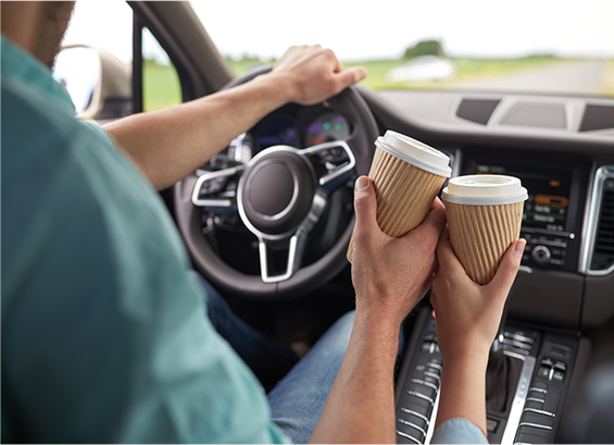 RETAIL Image of a couple in a car toasting with two takeout coffee cups