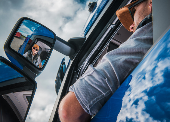 CAREERS Image of a young man driving a truck while looking in his driver side mirror